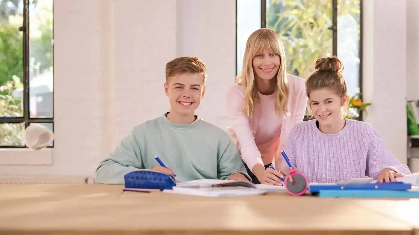 Eine Nachhilfelehrerin der Schülerhilfe schaut in die Kamera während eine Schülerin und ein Schüler in der Schülerhilfe lernen.