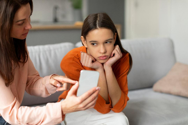 Kind schaut traurig auf ihr Smartphone, die Mutter sitzt daneben. Das Kind möchte gerne ein Produkt ihrer Lieblingsinfluencerin haben, die Mutter ist dagegen. 