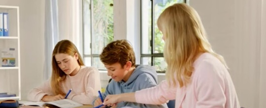Eine Frau hilft zwei Kindern beim Mathe-Lernen.