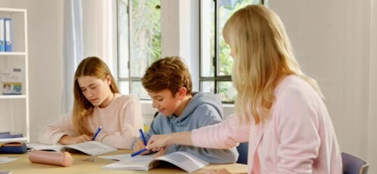 Eine Frau hilft zwei Kindern beim Mathe-Lernen.